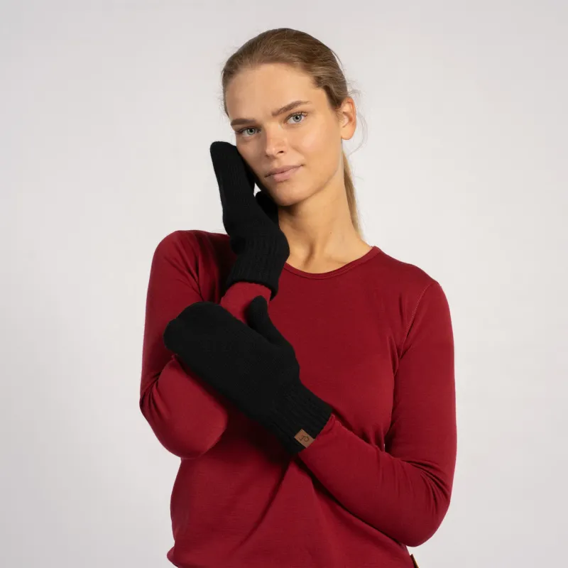 Woman posing in black knitted merino wool mittens with a red long-sleeve top, hand resting on face.
